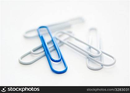 Blue paper clip standing out from group of white ones.