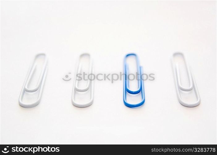 Blue paper clip with collection of white ones.