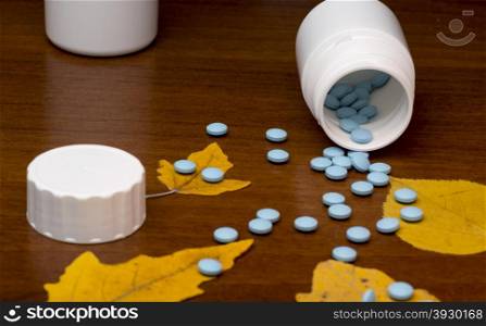 Blue pills and medicine bottle on wooden background. Blue pills and medicine bottle on wooden background with autumn leafs
