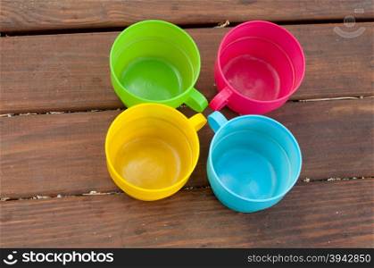 Blue, pink, green and yellow cups staying circle on wooden table