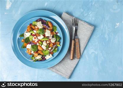 Blue plate of fresh superfoods healthy salad with red onion, tomatoes, doucette (lambs lettuce, corn salad, field salad) and feta cheese. Light blue surface, top view, flat lay, copy space.