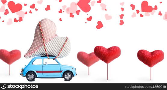 Blue retro toy car delivering craft heart for Valentine's day on white background with flying hearts