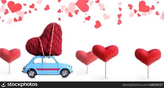 Blue retro toy car delivering craft heart for Valentine's day on white background with flying hearts