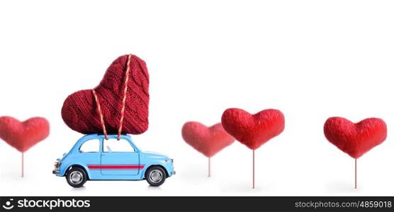 Blue retro toy car delivering craft heart for Valentine's day on white background