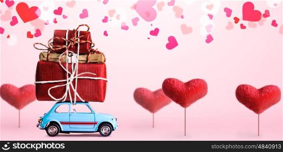 Blue retro toy car delivering gift box for Valentine's day on pink background with heart trees