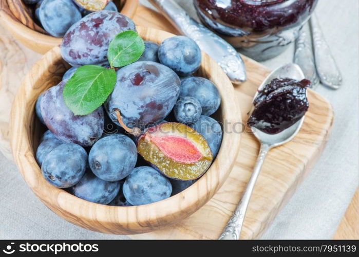 Blue ripe plums in wooden bowl and jam in a glass jar