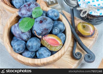 Blue ripe plums in wooden bowl and jam in a glass jar