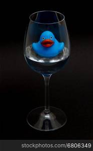 Blue rubber duck in a wineglass with water (black background)