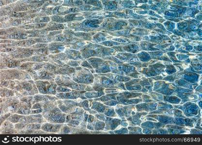 Blue sea flowing water surface with waves and some pebbly bottom view. Abstract background pattern.