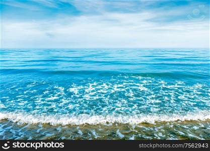 Blue sea water with waves, foam and white clouds on the sky. Calm tropical landscape