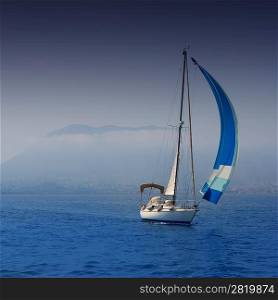 Blue sea with sailboat sailing in a foggy coast in mediterranean sea