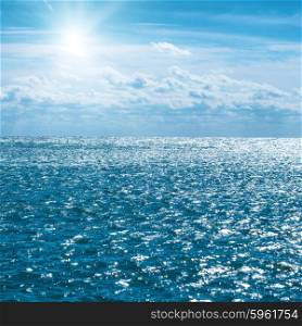 Blue sea with sky, sun and clouds. Water natural background