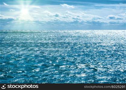 Blue sea with sky, sun rays and clouds. Water natural background