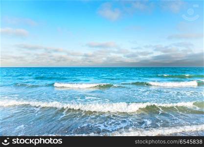 Blue sea with waves, foam and white clouds on the sky. Blue sea with waves