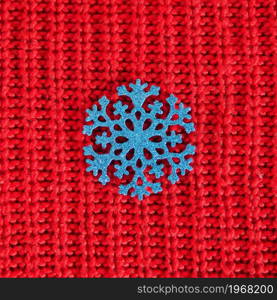 blue shiny snowflake on a red knitted background.