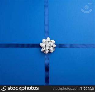 blue silk ribbon crossed on a dark blue background, in the middle a silver bow, imitation of tying a gift, top view