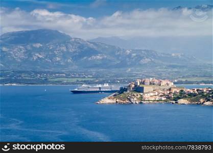 Blue skies over the The citadel of Calvi with a cruise liner in port and mountains in the distance