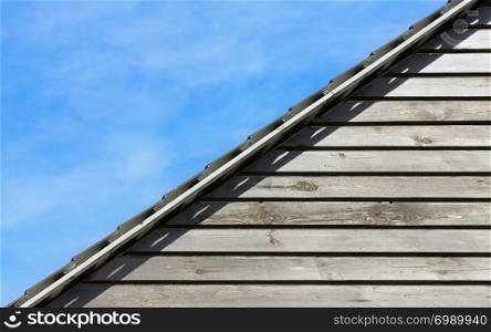 Blue sky and diagonally located part of a wooden wall with horizontal panels under the roof close-up. Old wood planks texture and natural background for text with space for copy.