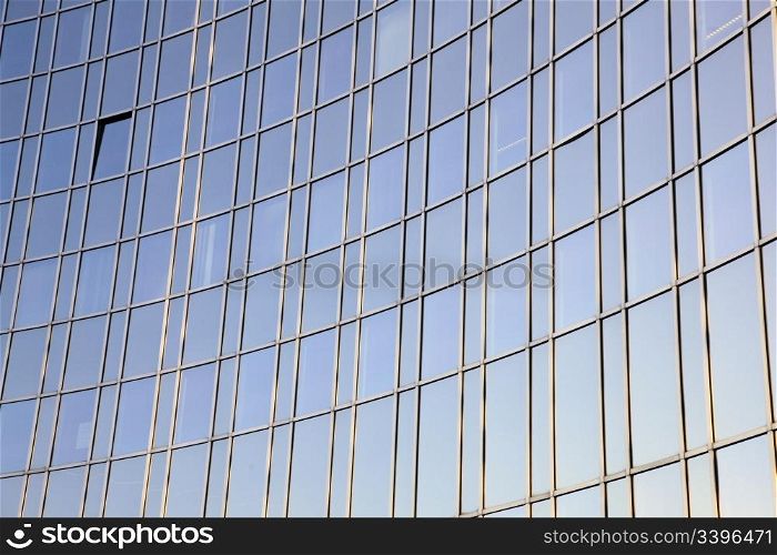 blue sky reflected in curved facade of glass and steel
