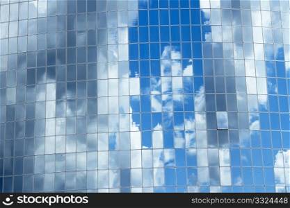 Blue sky with clouds reflected in glass windows of skyscrapers in the big mirror as