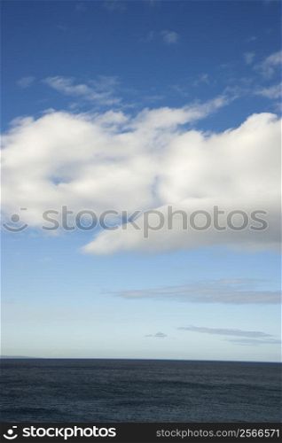 Blue sky with fluffy white clouds over ocean horizen.
