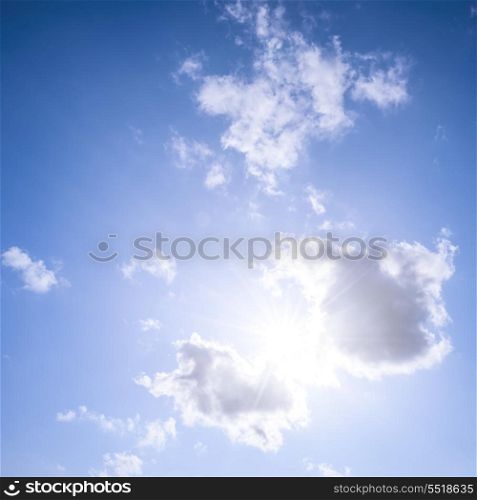 Blue sky with sun and clouds. Square blue sky background with bright sun flare shining through clouds