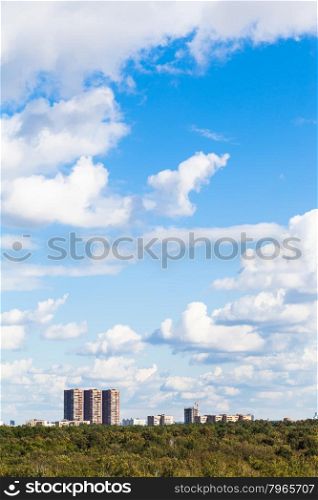 blue sky with white clouds over urban buildings and green forest in summer