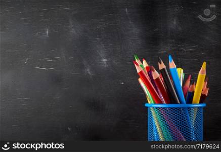 blue stationery glass with multi-colored wooden pencils and pens, chalkboard background, copy space