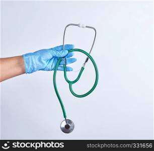 blue sterile gloved hand holding a green medical stethoscope on white background