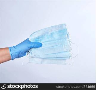 blue sterile gloved hand holding a medical mask on a white background
