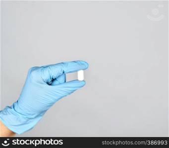 blue sterile gloved hand holding a white pill on gray background