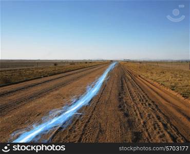 Blue streak of light on dirt road against clear sky