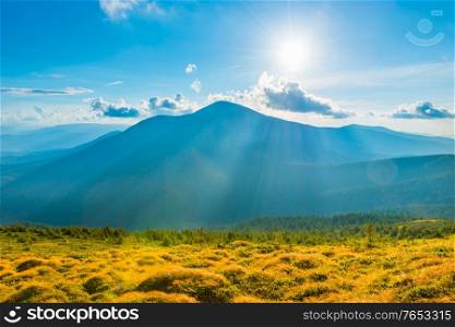 Blue sunset mountains landscape and grass meadow with sun rays