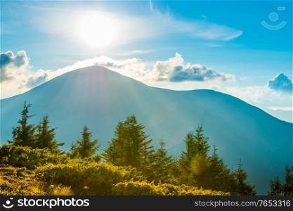 Blue sunset mountains landscape and grass meadow with sun rays