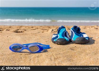Blue swimming goggles and water shoes lying at coast with sea