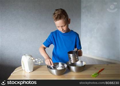 blue t-shirt, cooking, two bowls, metal bowls, pizza dough, mix ingredients, kitchen work, wooden table, baking, baby in the kitchen, trying dough, finger in mouth, mixer, cooking, dessert, pastry chef, pawar, kitchen, dishes, spoon, mixer, kneading. The child prepares dough in metal bowls and looks away . Pour flour