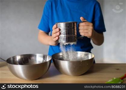 blue t-shirt, cooking, two bowls, metal bowls, pizza dough, mix ingredients, kitchen work, wooden table, baking, baby in the kitchen, trying dough, finger in mouth, mixer, cooking, dessert, pastry chef, pawar, kitchen, dishes, spoon, mixer, kneading. A child prepares dough in metal bowls. Sift the flour. Hands