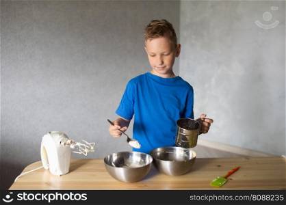 blue t-shirt, cooking, two bowls, metal bowls, pizza dough, mix ingredients, kitchen work, wooden table, baking, baby in the kitchen, trying dough, finger in mouth, mixer, cooking, dessert, pastry chef, pawar, kitchen. The child prepares dough in metal bowls and looks away . Pour flour