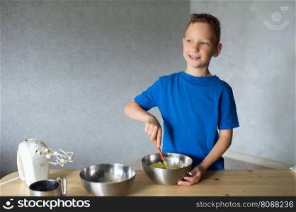 blue t-shirt, cooking, two bowls, metal bowls, pizza dough, mix ingredients, kitchen work, wooden table, baking, baby in the kitchen, trying dough, finger in mouth, mixer, cooking, dessert, pastry chef, pawar, kitchen. The child prepares dough in metal bowls and looks away . mix the ingredients
