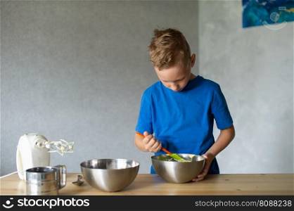 blue t-shirt, cooking, two bowls, metal bowls, pizza dough, mix ingredients, kitchen work, wooden table, baking, baby in the kitchen, trying dough, finger in mouth, mixer, cooking, dessert, pastry chef, pawar, kitchen. A child prepares dough in metal bowls. mix the ingredients