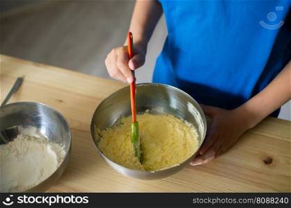 blue t-shirt, cooking, two bowls, metal bowls, pizza dough, mix ingredients, kitchen work, wooden table, baking, baby in the kitchen. A child prepares dough in metal bowls. Without a face