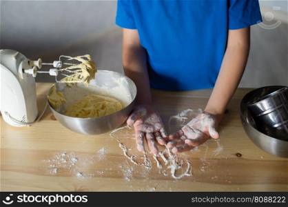 blue t-shirt, cooking, two bowls, metal bowls, pizza dough, mixing ingredients, kitchen work, wooden table, baking, child in the kitchen, mixer in a plate, children&rsquo;s hands, cooking, dessert, pastry chef, pavar, kitchen. The child prepares the dough for baking by scattering flour. Hands in flour