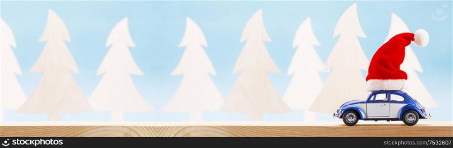 Blue toy car with Christmas Santa Claus hat on wooden forest background , copy space for text. Toy car with Santa hat
