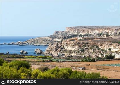 blue tropical ocean and big rocks with green plants in foreground on the spanish island Malta