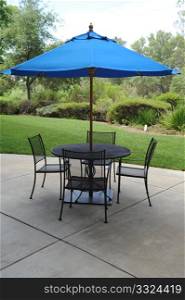 Blue umbrella, table and chairs on a patio in a graden setting. Wrought Iron Table With Umbrella