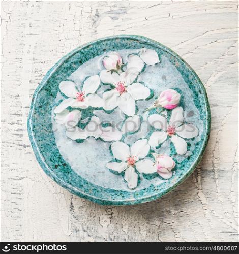 Blue water bowl with lovely spring blossom on light shabby chic background, top view. Spa and wellness concept