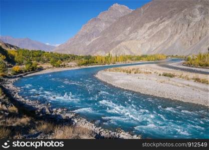 Blue water of winding Gilgit river of Indus flowing through Gupis, Ghizer with mountains and autumn forest. Gilgit Baltistan, Pakistan.