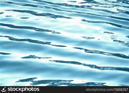Blue water surface with waves and sun light reflections.