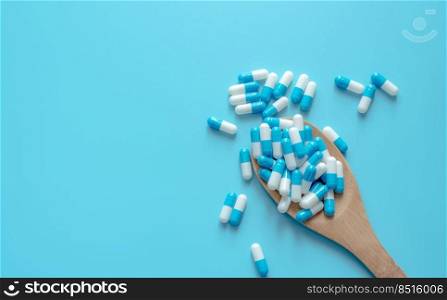 Blue-white capsule pills on wooden spoon. Capsule pills on blue background. Health topics. Drug for treatment illness. Medication use. Medical care. Pharmaceutical industry. Capsule pill production.