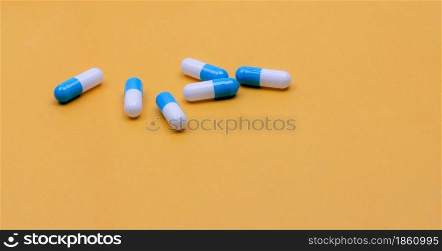 Blue-white capsules pill on yellow background. Pharmacy banner. Capsule pills manufacturing industry. Pharmaceutical industry. Drug development and new drug research concept. Capsule pills industry.